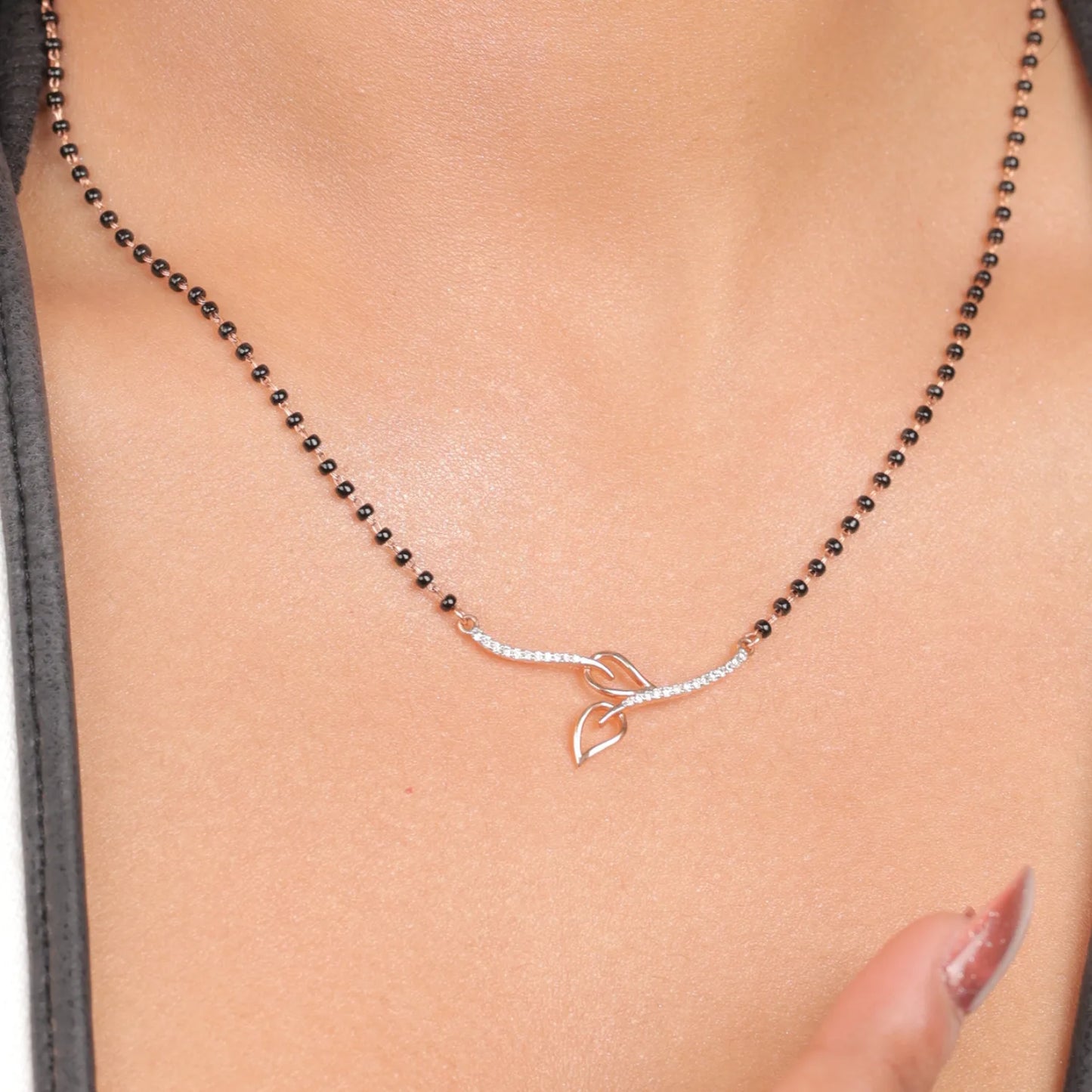 Close-up view of a jnjbymadhuri mangalsutra, showcasing its delicate black beaded chain and modern twin-leaf gold pendant design, worn gracefully on the neck for a timeless, elegant look.
