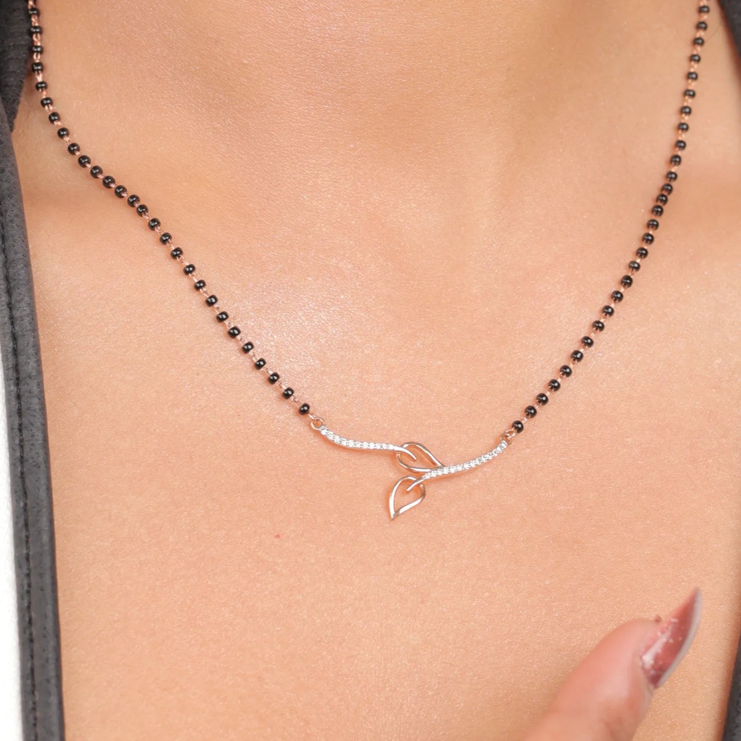 Close-up view of a jnjbymadhuri mangalsutra, showcasing its delicate black beaded chain and modern twin-leaf gold pendant design, worn gracefully on the neck for a timeless, elegant look.
