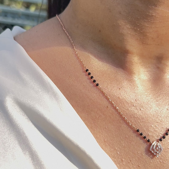 Close-up view of a minimalist mangalsutra in rose gold with black beads and a dainty diamond swirl pendant, capturing elegance in sunlight. A timeless creation by jnjbymadhuri.
