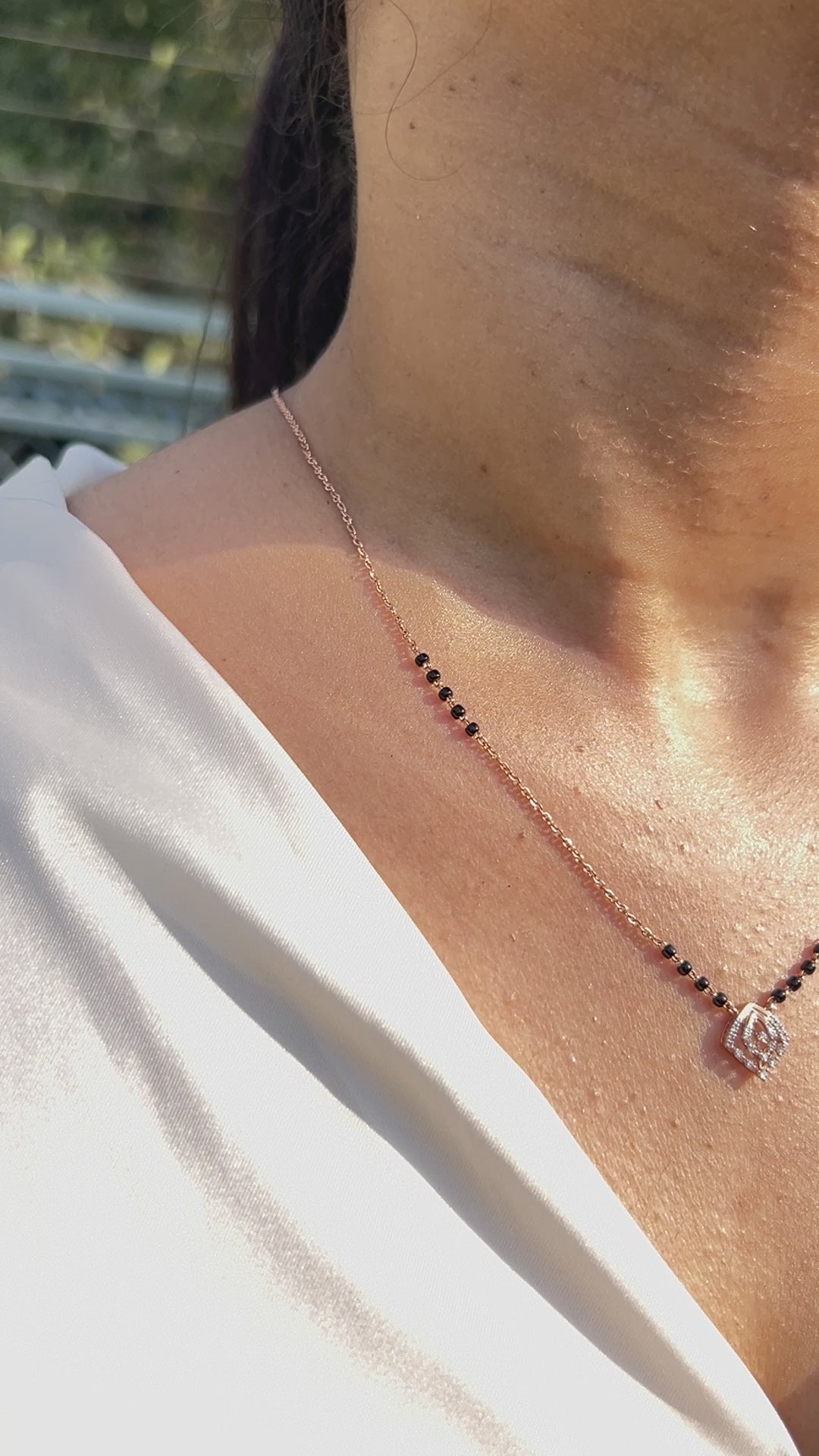 Close-up view of a minimalist mangalsutra in rose gold with black beads and a dainty diamond swirl pendant, capturing elegance in sunlight. A timeless creation by jnjbymadhuri.
