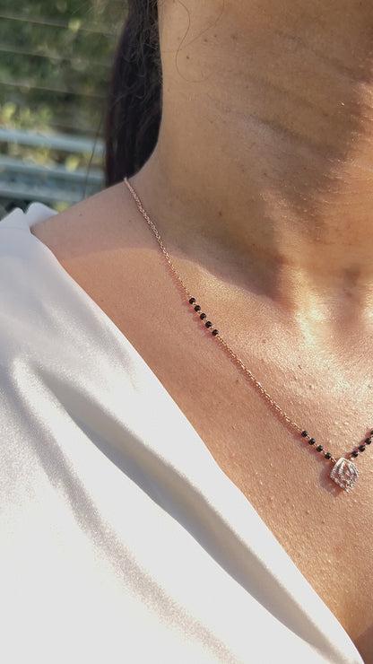 Close-up view of a minimalist mangalsutra in rose gold with black beads and a dainty diamond swirl pendant, capturing elegance in sunlight. A timeless creation by jnjbymadhuri.
