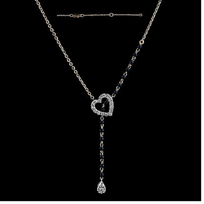 A stylish and elegant diamond heart mangalsutra by jnjbymadhuri, featuring a sparkling heart-shaped pendant encrusted with diamonds, complemented by a delicate drop-shaped diamond hanging below. The necklace combines a traditional black bead chain on one side with a sleek gold chain on the other, creating a modern, asymmetrical design perfect for contemporary Indian fashion.
